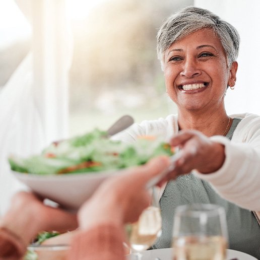 Smiling woman grabbing salad bowl across the table
