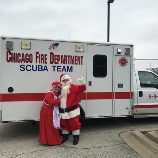 Dentist dressed as Santa Claus posing with Misses Claus in front of Chicago Fire Department Scuba Team truck
