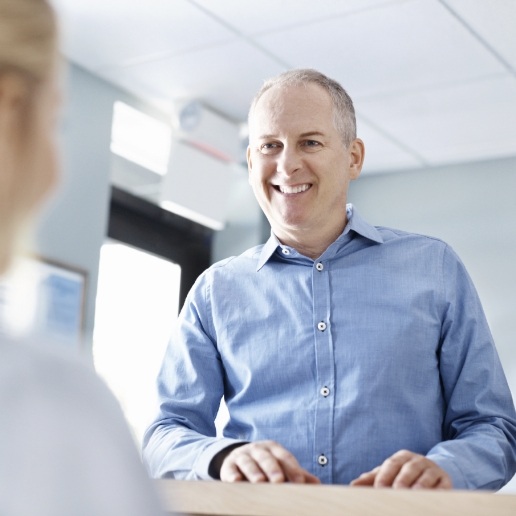 Man in light blue collared shirt talking to dental team member at front desk