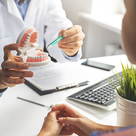 Dentist holding a set of dentures while talking to a patient at a desk