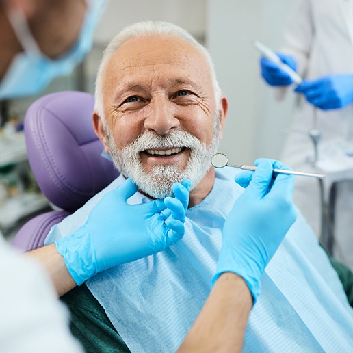 Man with white hair and beard in dental chair smiling at dentist