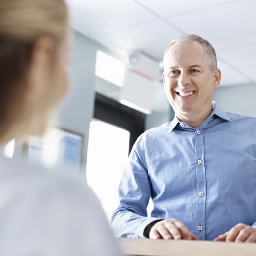 Man in light blue collared shirt talking to dental team member at front desk