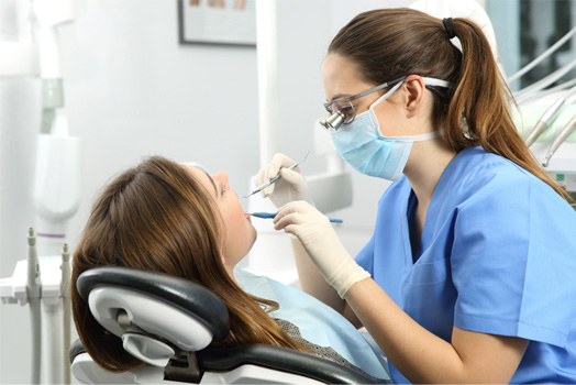 Dentist in blue scrubs examining patient’s teeth