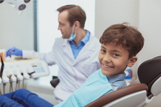 Boy in dental chair smiling at camera with dentist blurry in background