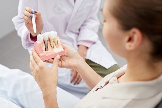 Dentist pointing with pen to sample implant patient is holding