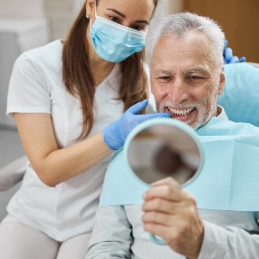 Senior dental patient looking at his new smile in a hand mirror