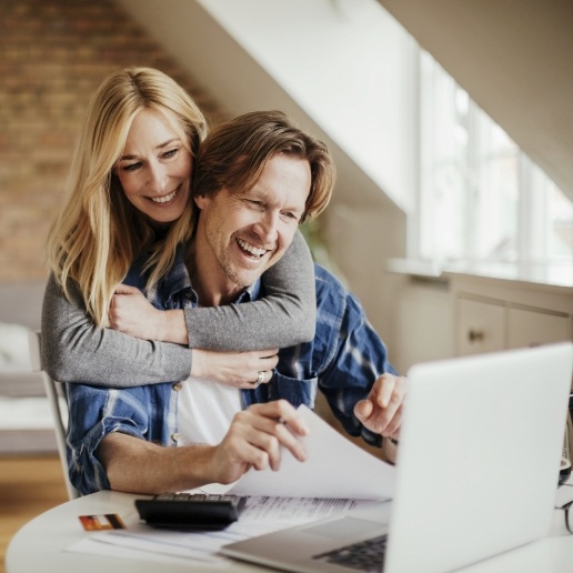 Woman hugging man from behind while he sits at computer reading dentist reviews in Merrillville