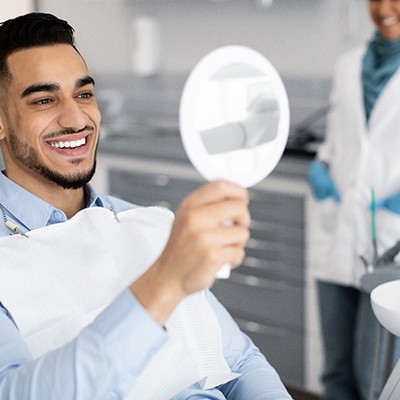 Man with veneers smiling at reflection in handheld mirror