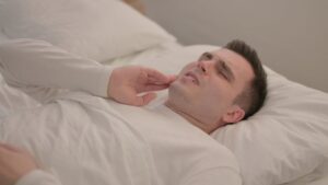 Man holding jaw in pain in bed at night.